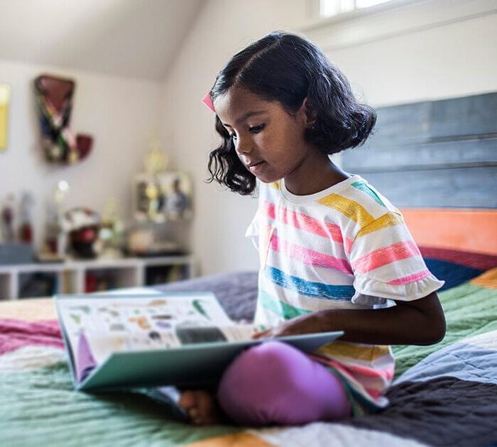 Elementary student reading a book in bed - Connections Academy